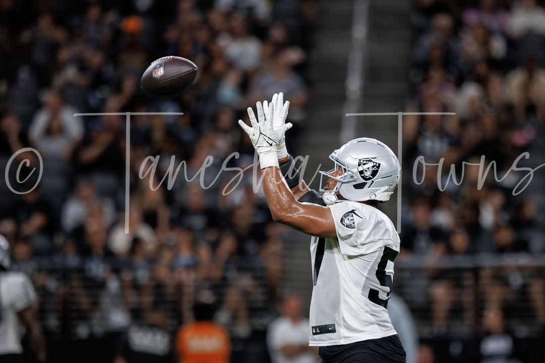 Raiders player in white uniform reaches up with both hands to catch a football during an indoor NFL game.
