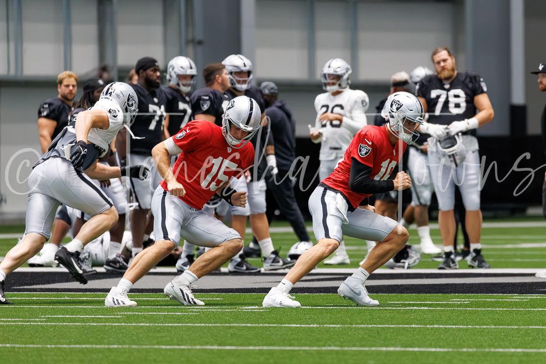 Las Vegas Raiders quarterbacks in red jerseys run drills during indoor training camp practice.