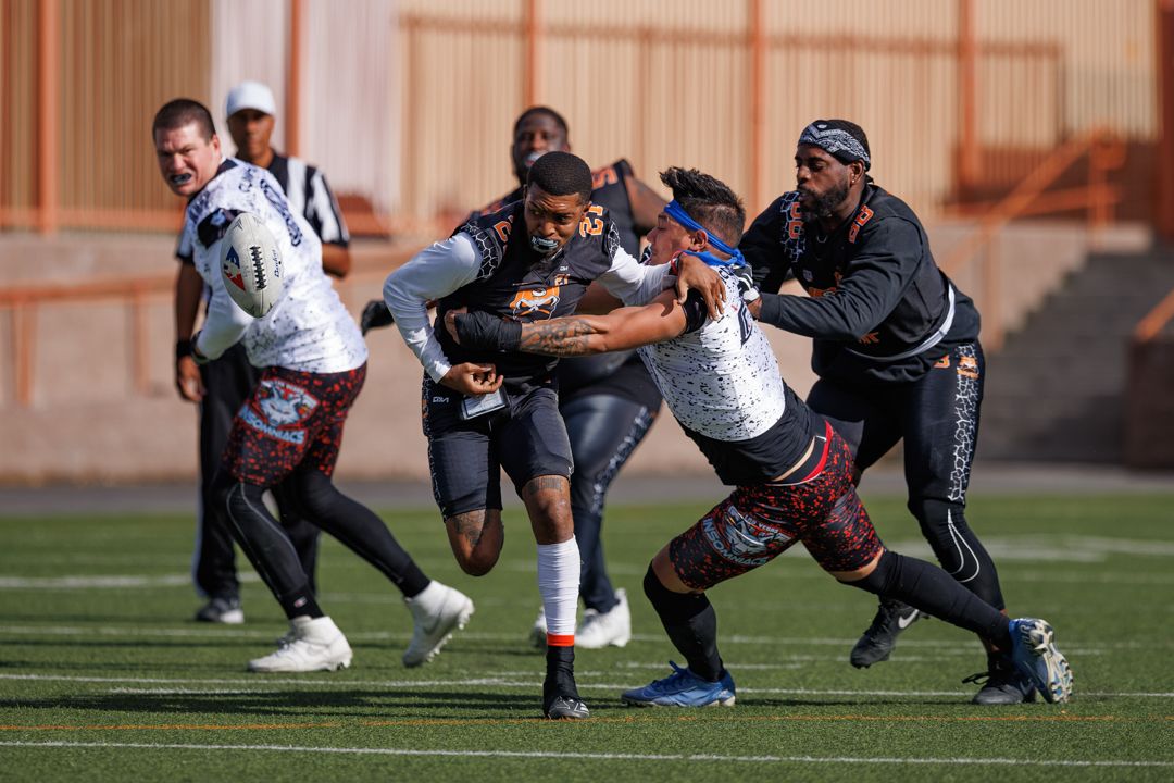 Rugby players compete during an intense tackle sequence on a turf field in a daytime outdoor match.