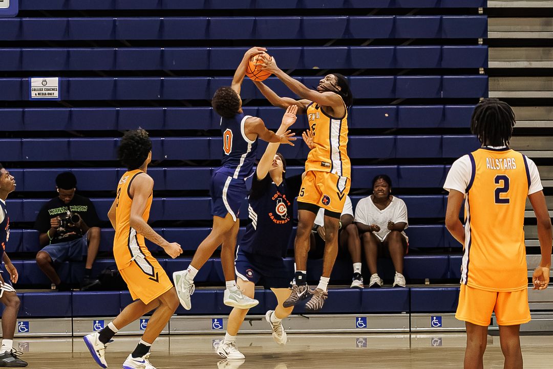 Basketball players in yellow and blue uniforms compete for the ball during an indoor high school basketball game.