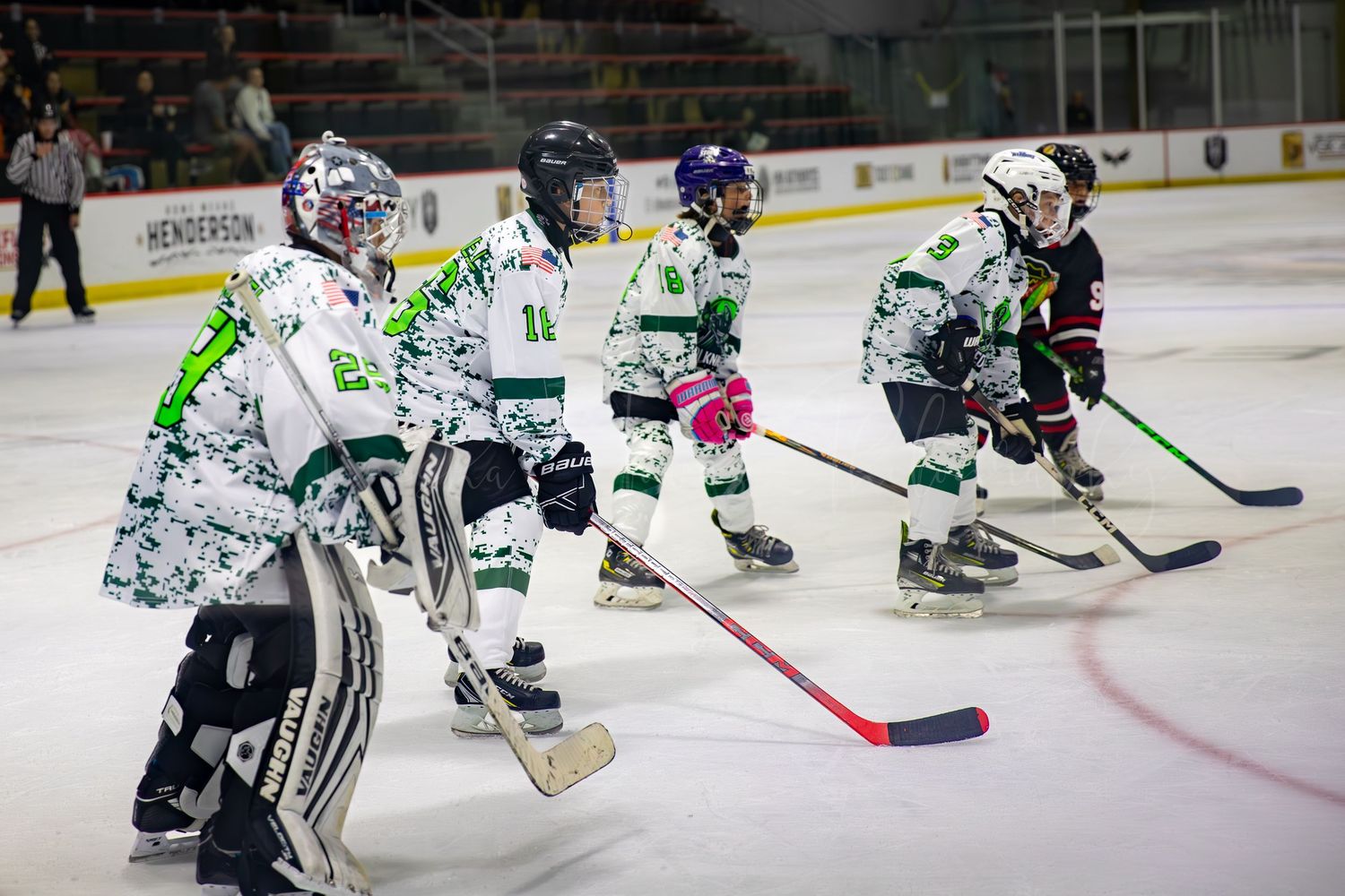 Youth hockey players in white and green jerseys line up on ice during practice session.