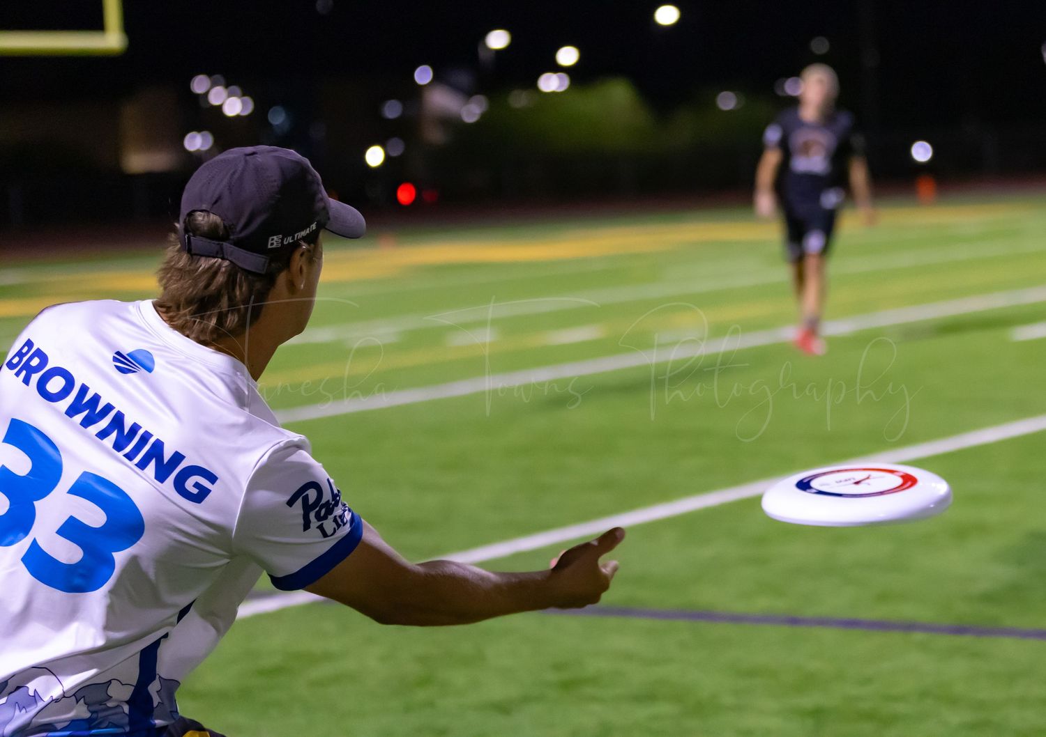 Ultimate frisbee player in white jersey throws a disc during a nighttime game.