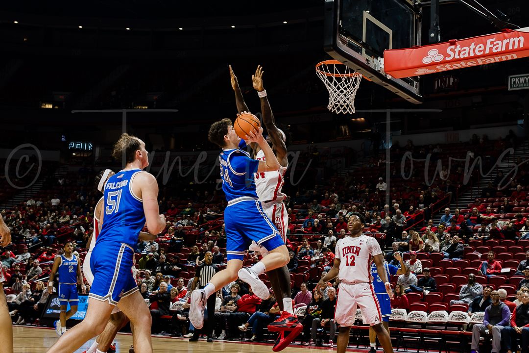 Basketball player drives to the hoop for a layup against defenders in a college basketball game.