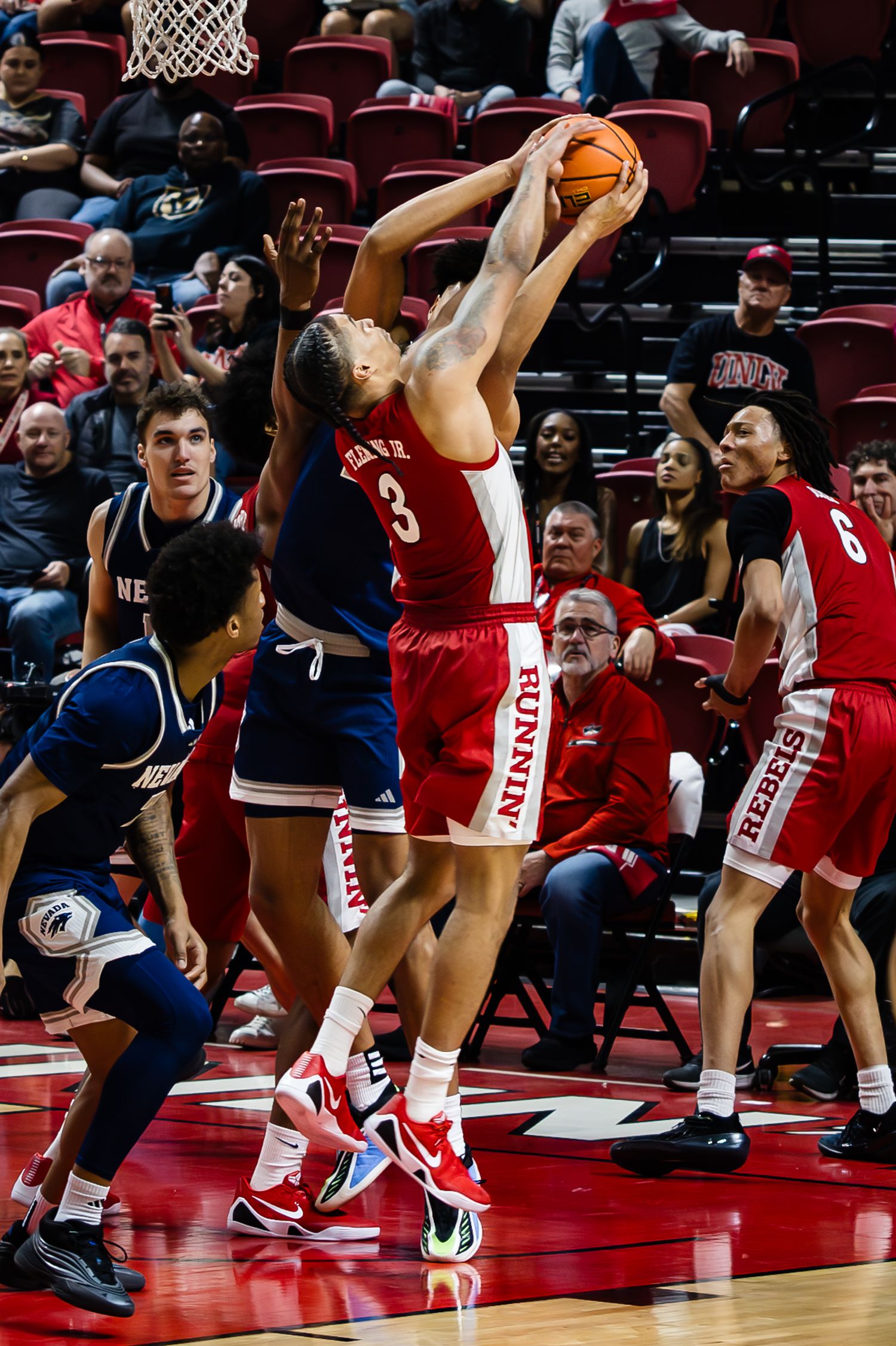 UNLV Runnin' Rebels player #3 battles for a rebound against Nevada Wolf Pack defenders during a college basketball game.