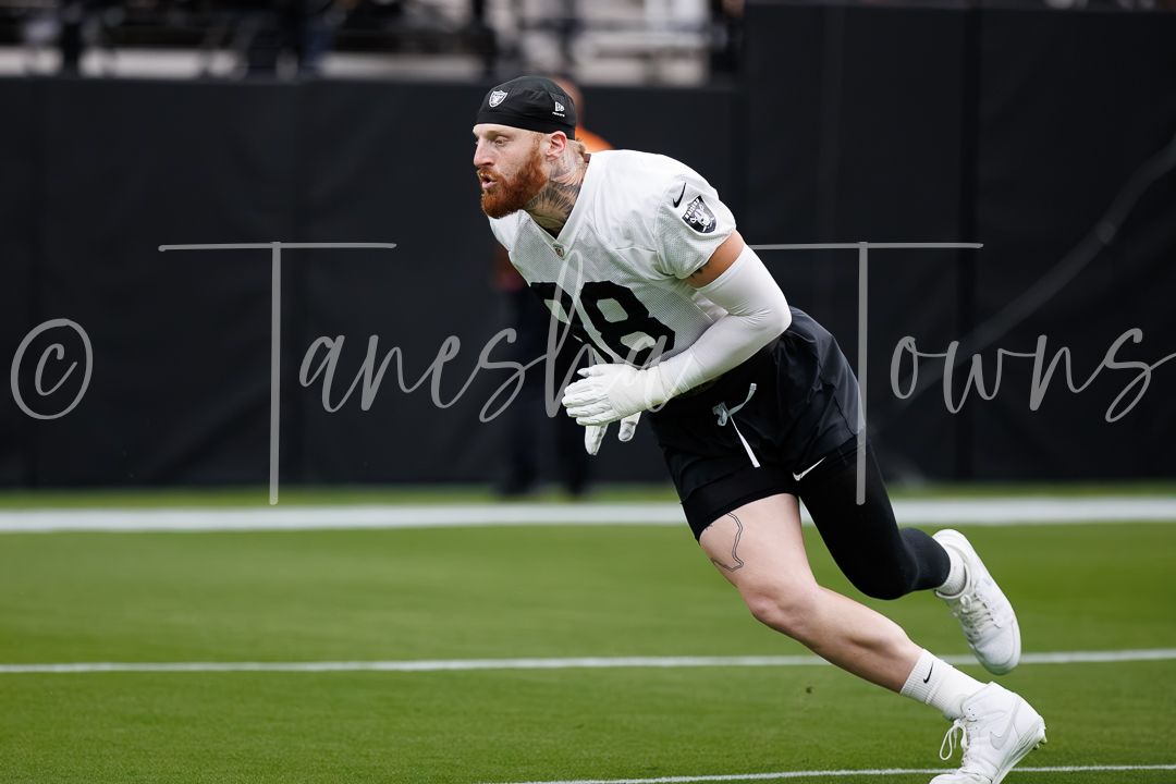 Football player in black and white uniform sprinting on green field during NFL practice session.