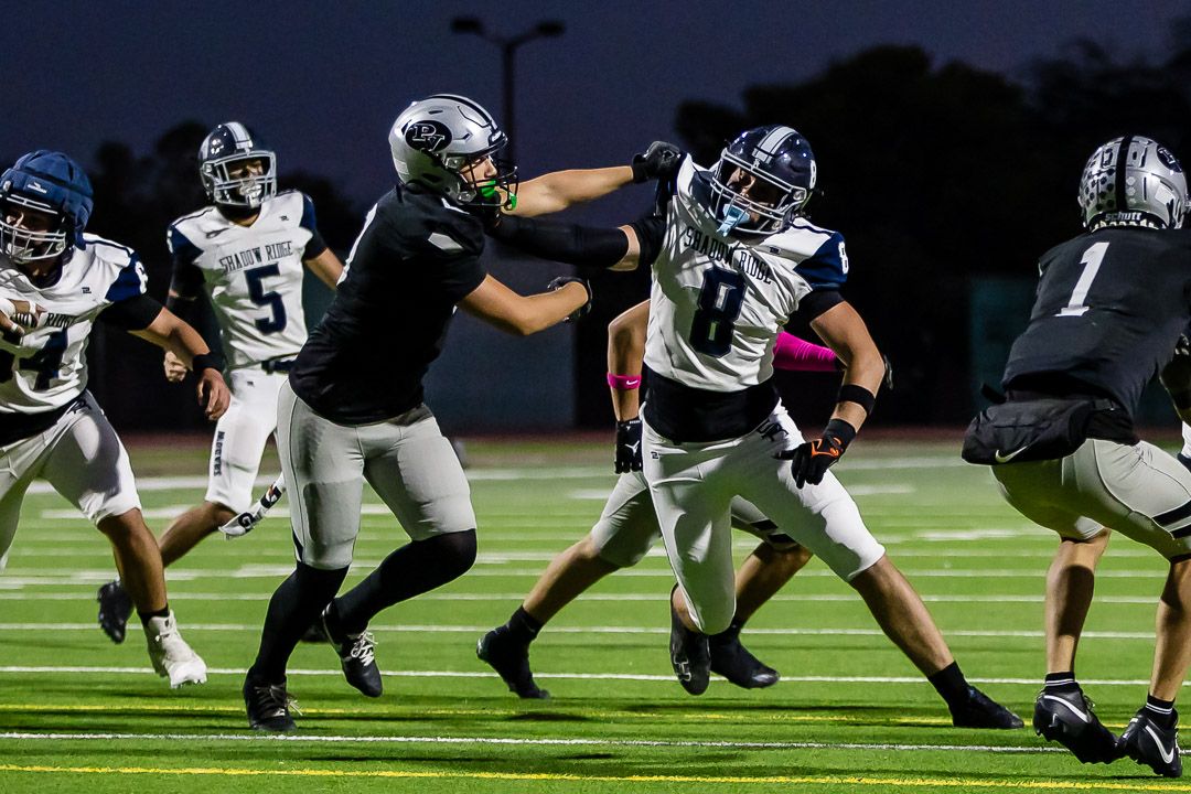 Football players in offensive and defensive formations prepare for the snap during an evening match.