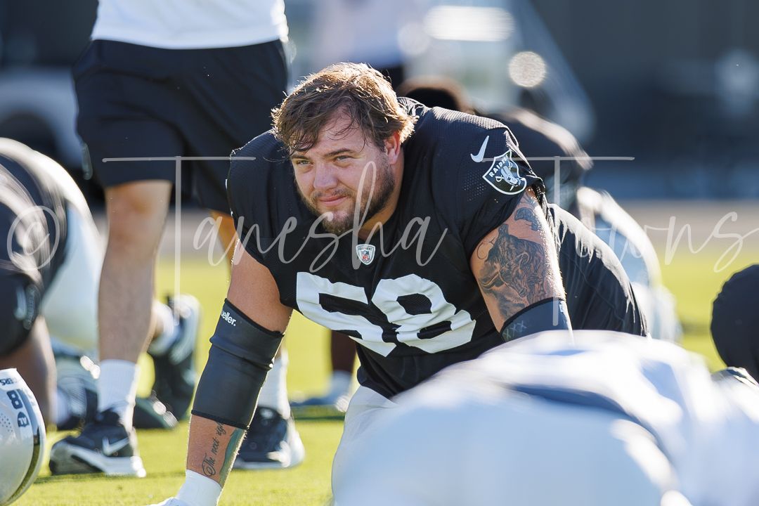 Football player wearing jersey number 58 crouches in stance during NFL training camp practice on outdoor field.