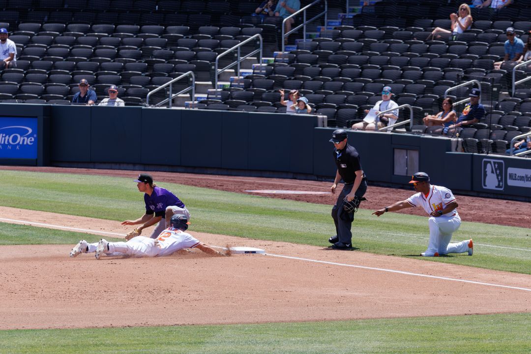 Baseball player dives back to first base as fielder applies tag during MLB game with umpire watching.