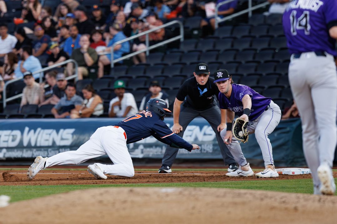 Baseball player slides into third base as fielder reaches to tag during a professional minor league game.