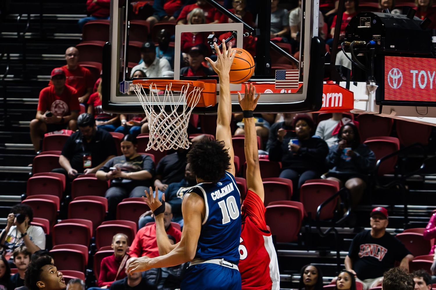Basketball player #10 attempts a layup while defender blocks during an indoor college basketball game.