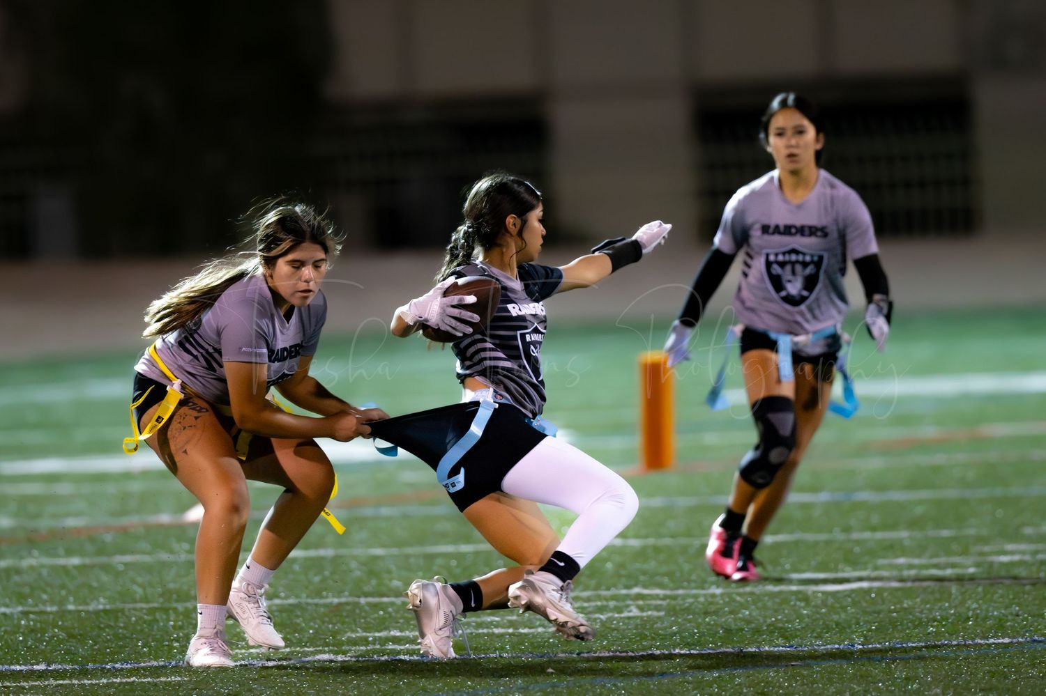 Flag football players compete on a nighttime field with dramatic lighting.