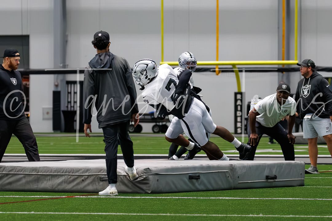 Raiders players practice drills on indoor turf field during NFL training camp session.