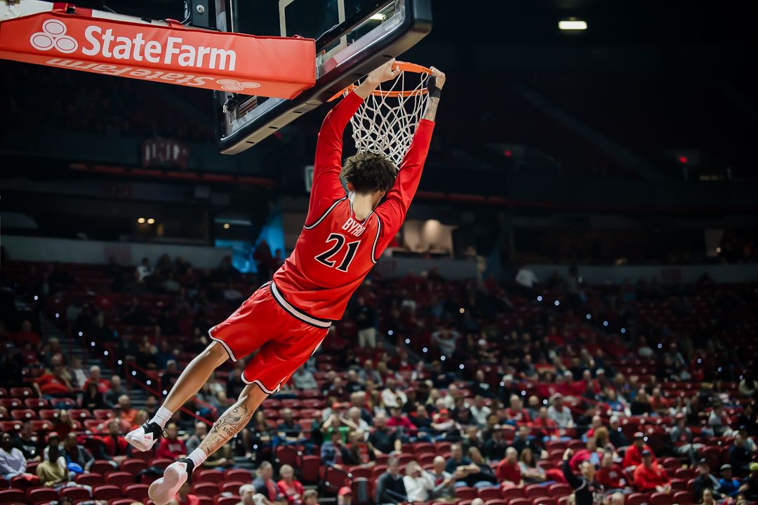 Basketball player in red Chicago Bulls uniform soars through the air for a powerful slam dunk during game action.
