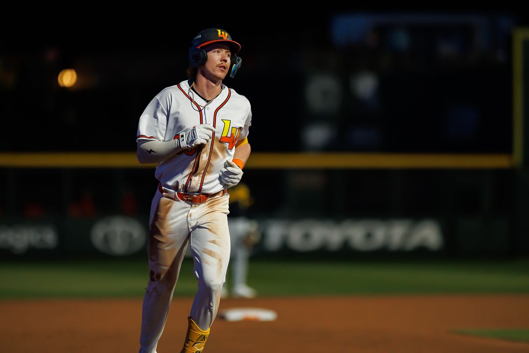 Baseball player in yellow and white uniform rounds the bases at night under stadium lights.
