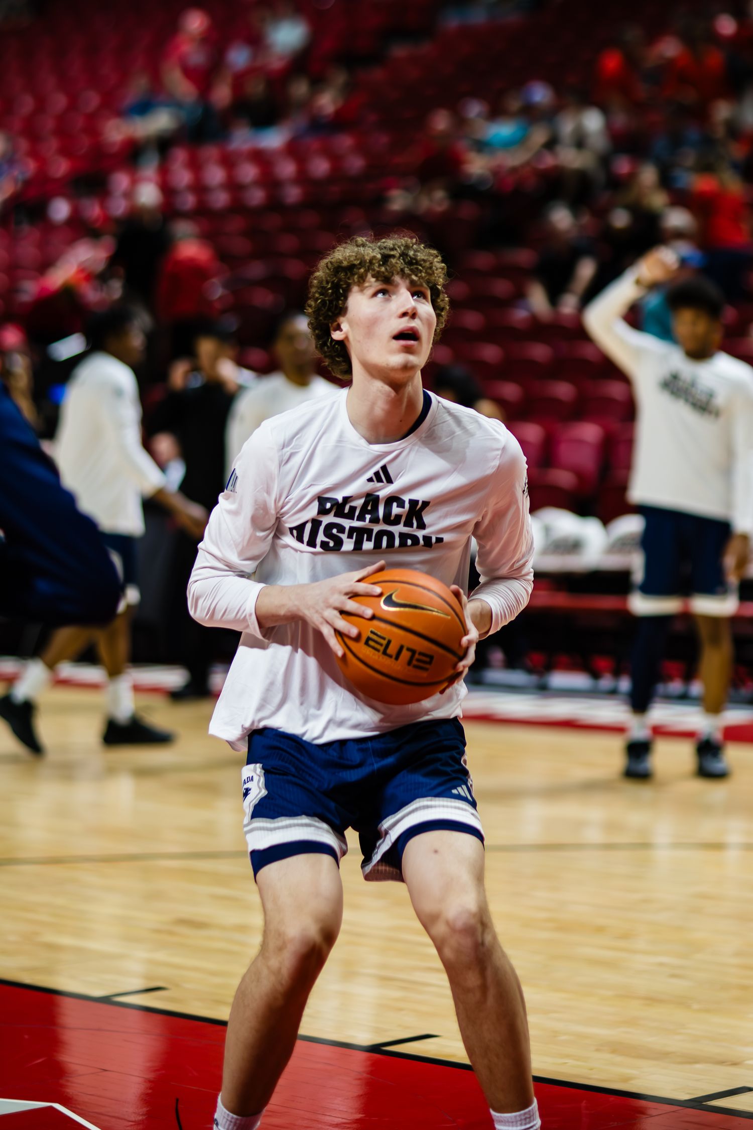 Young basketball player in white Adidas shirt prepares to shoot free throw during warm-ups on indoor court.