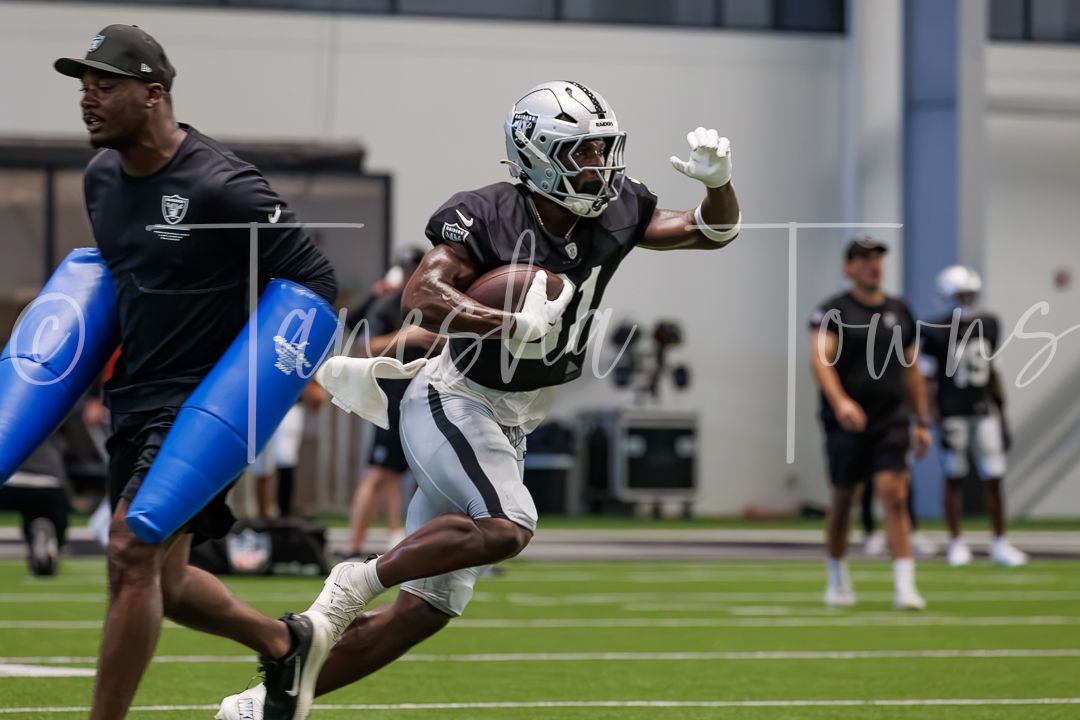 Raiders player runs with football during indoor practice drill.