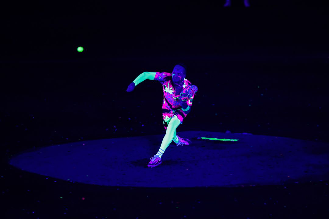 Performer dancing under UV black light in vibrant neon costume on dark stage during fluorescent light show.