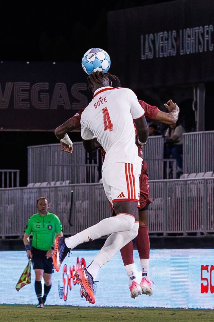 Soccer player #4 Boye leaps to head the ball during a Las Vegas Lights FC night match.