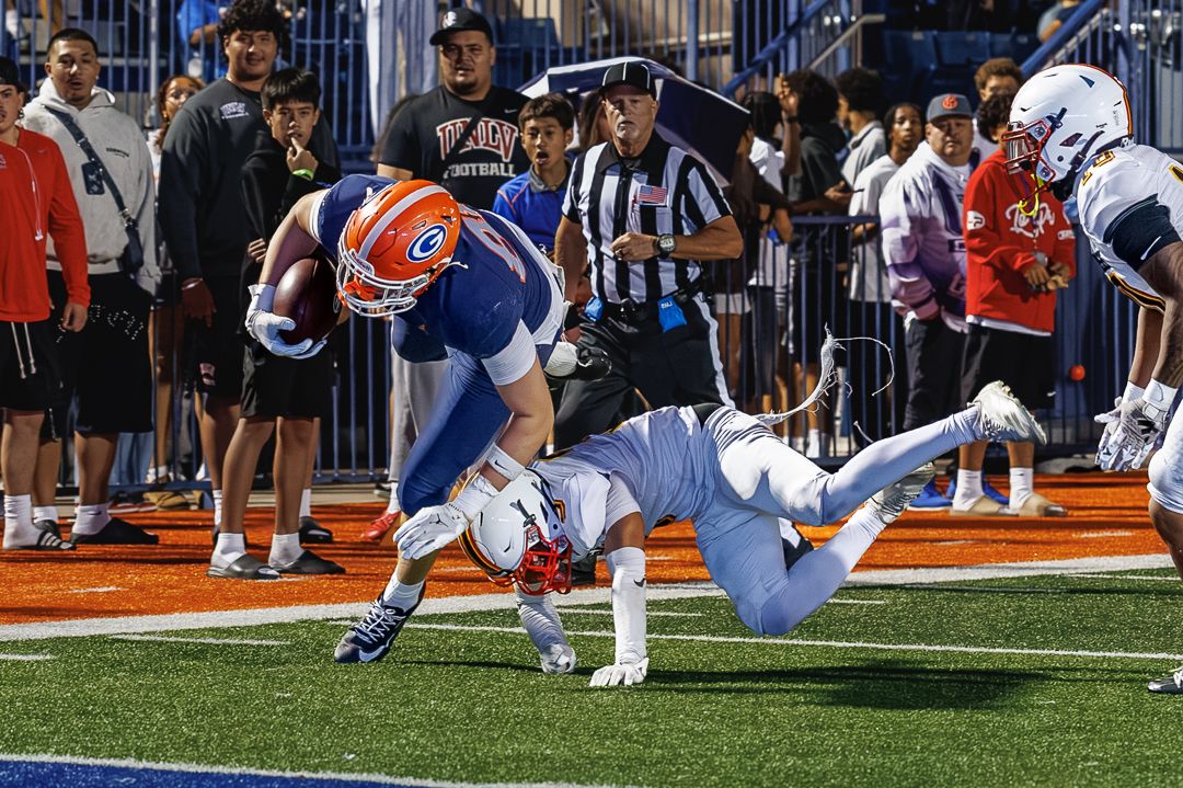 Football player in blue uniform dives into the end zone while being tackled during a high school football game.