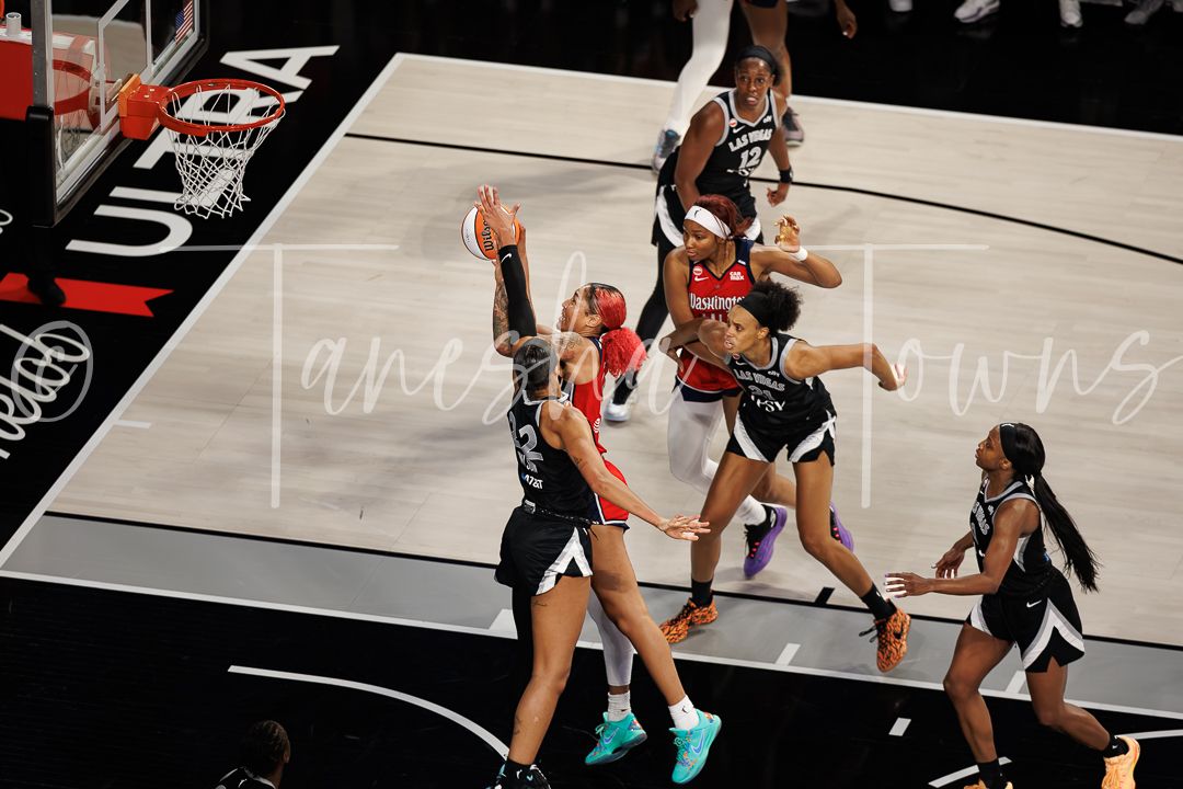 Multiple WNBA players battle for position under the basket during a competitive game.