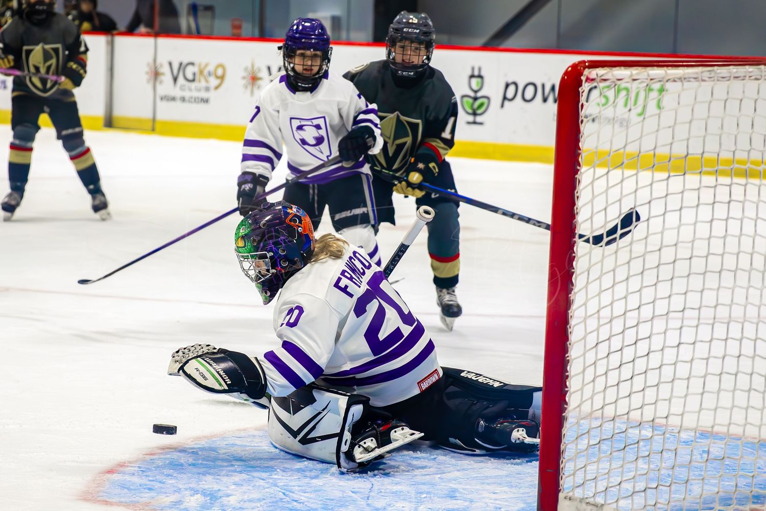 Hockey goalie in blue and white uniform makes diving save attempt during intense game action.