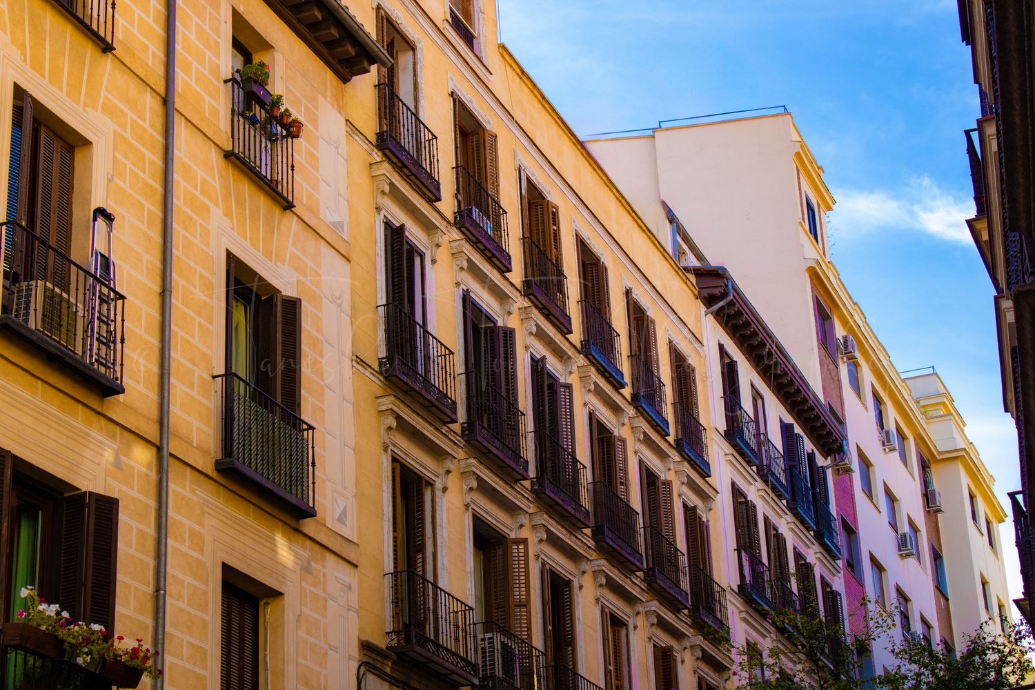 Historic yellow stone buildings with balconies along a narrow European street.