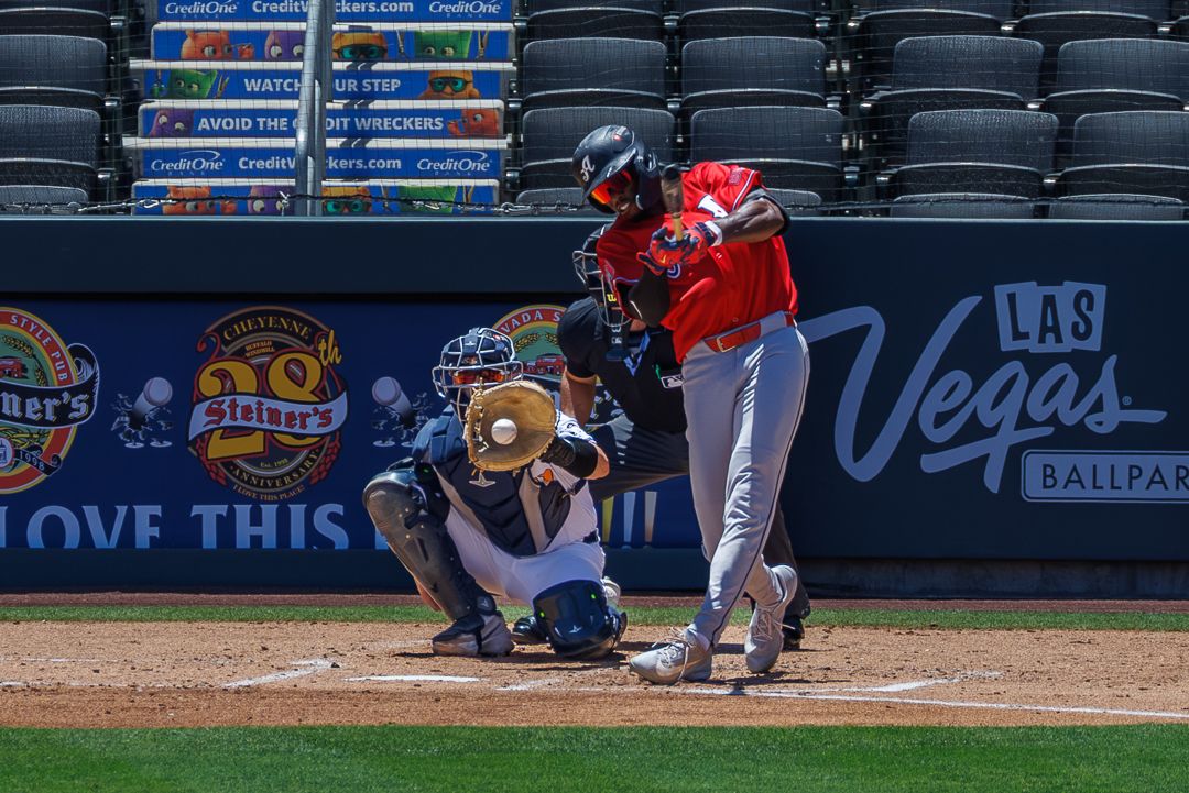 Baseball batter swings at pitch with catcher behind plate at Las Vegas Ballpark during MLB game.