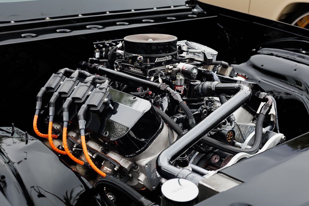 Close-up of a high-performance V8 engine with chrome details and orange spark plug wires in a classic car engine bay.