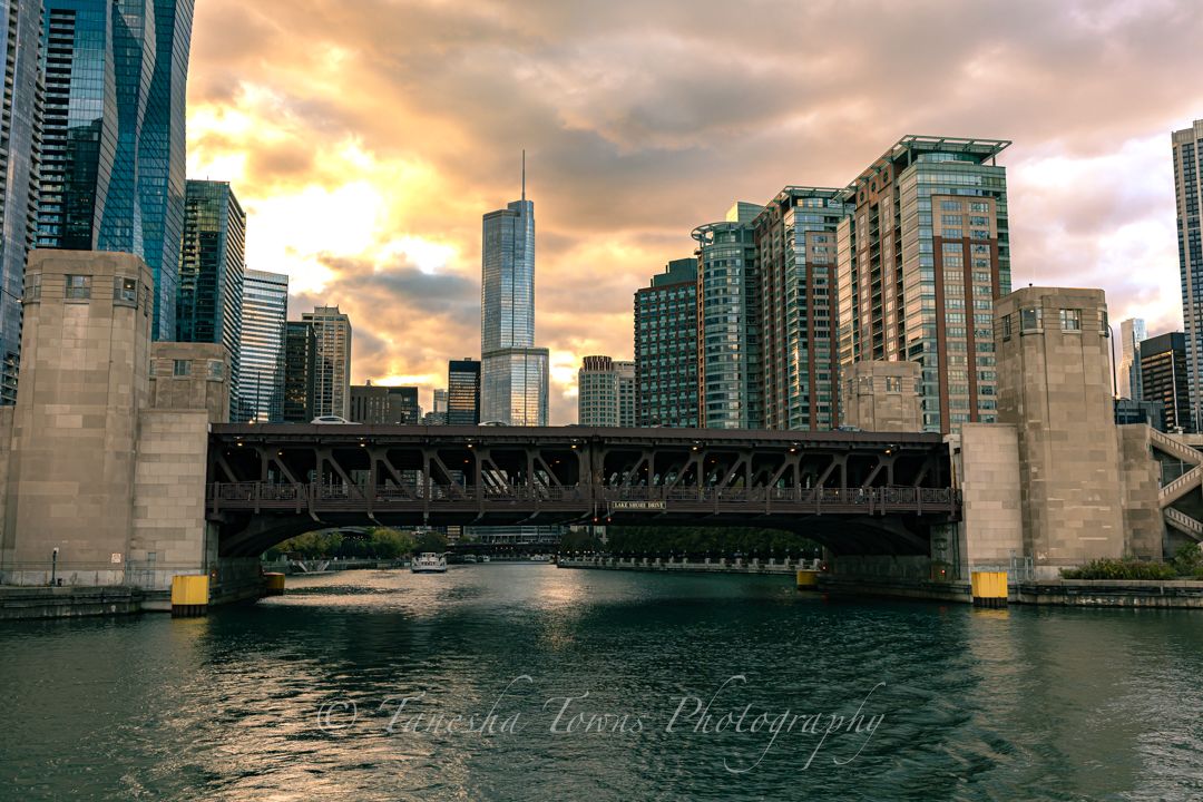 Historic bridge spans the Chicago River at sunset with dramatic clouds and urban architecture in the background.