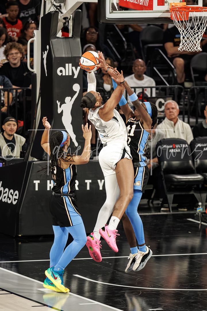 WNBA player jumps to grab rebound during intense game, defended by opponents in blue uniforms on indoor court.