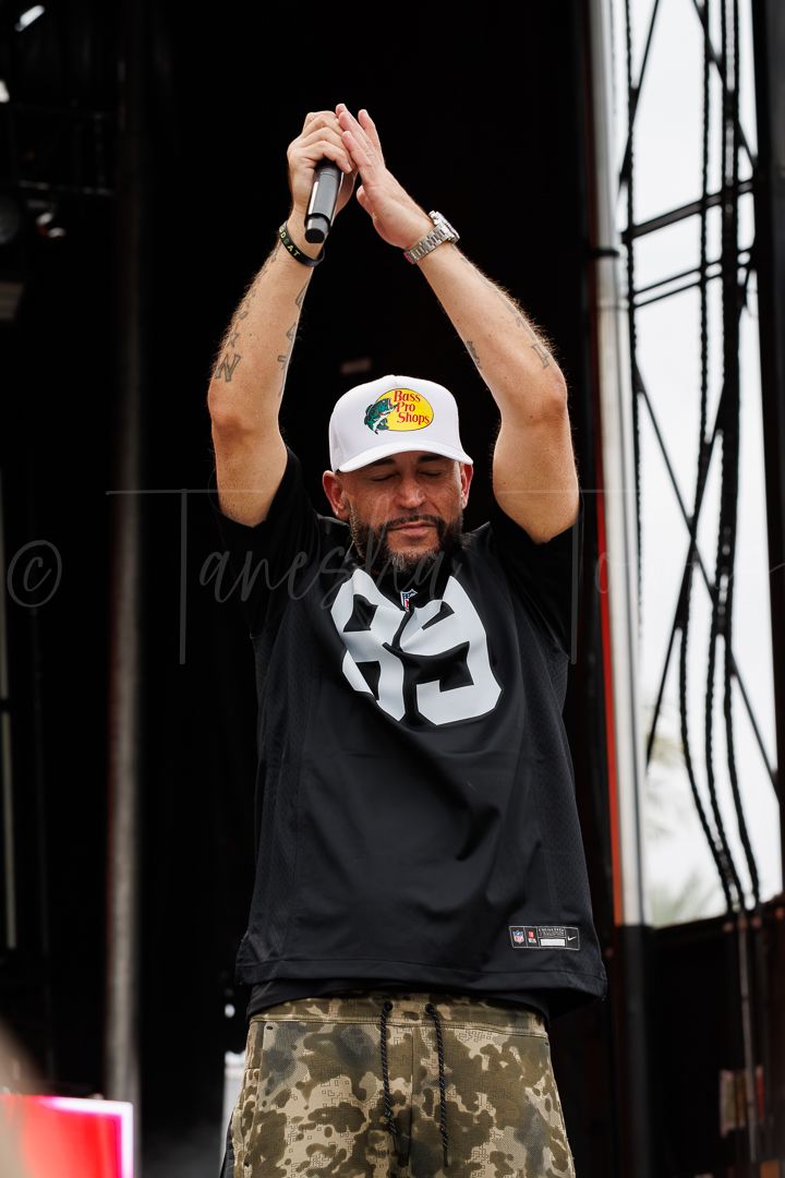 Male performer holding microphone overhead on outdoor stage wearing jersey 89.