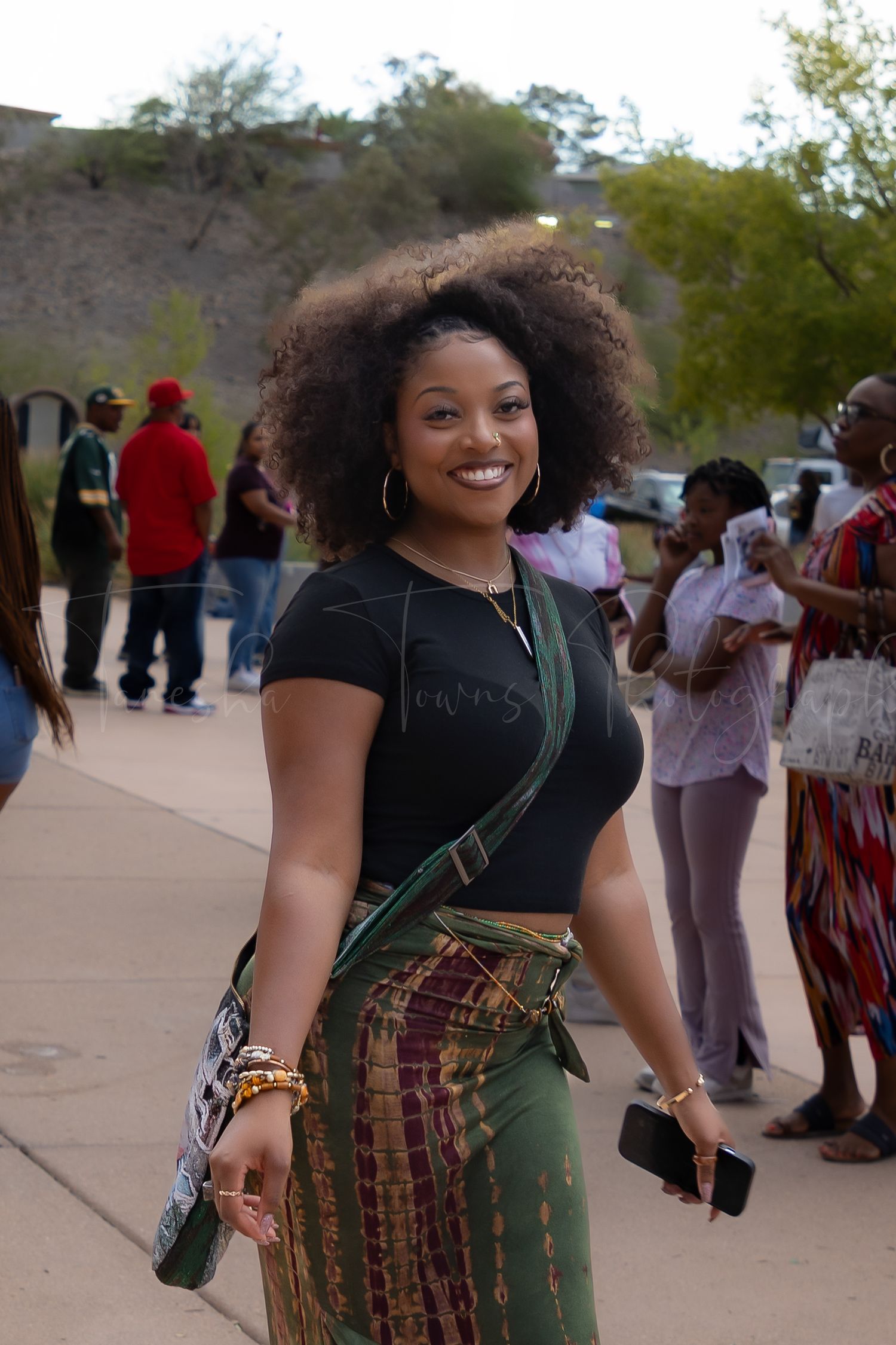 Person in patterned skirt and black top smiling at outdoor gathering.