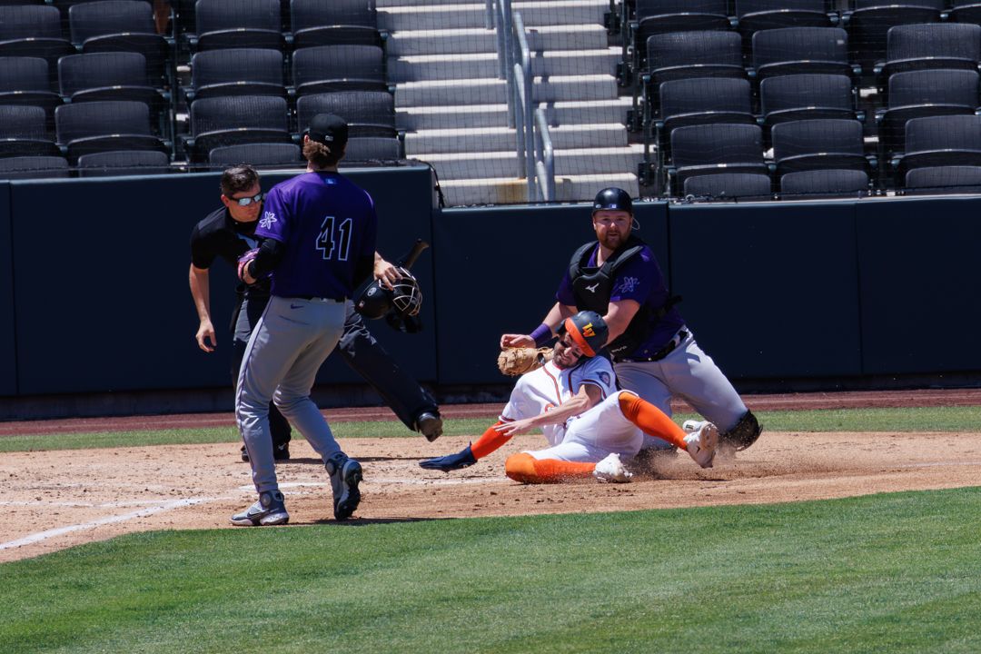 Baseball player sliding into home plate as catcher attempts tag during sunny daytime game in empty stadium.