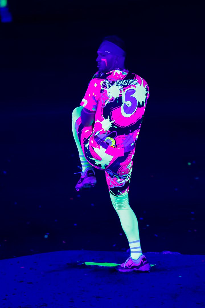 Person wearing neon pink Armstrong #3 jersey under UV blacklight, striking a dynamic pose on dark stage.