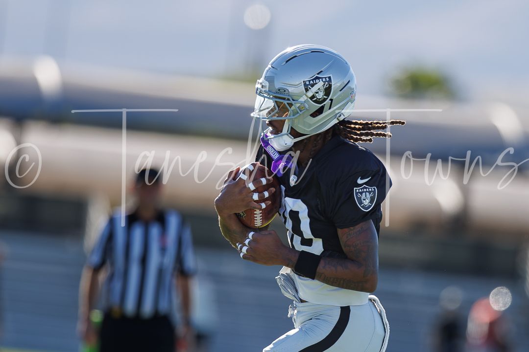 Raiders player in black jersey catches football during practice drill on sunny day.