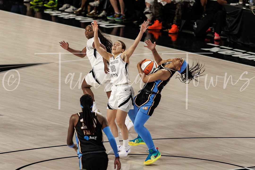 WNBA players battle for the ball during an intense basketball game, with athletes in white and blue uniforms competing.