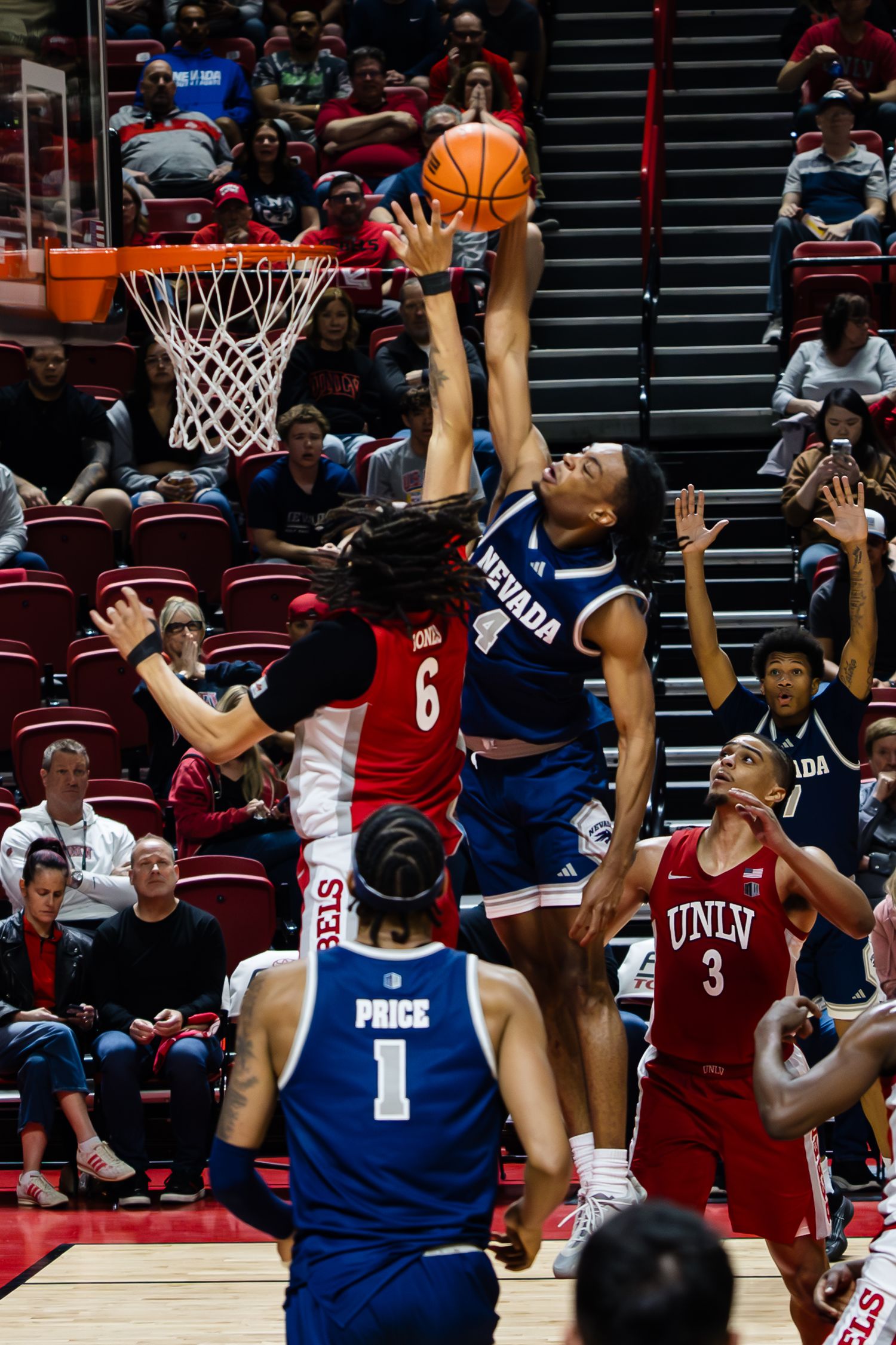 Nevada Wolf Pack player blocks a shot against UNLV Rebels during an intense college basketball game at a packed arena.