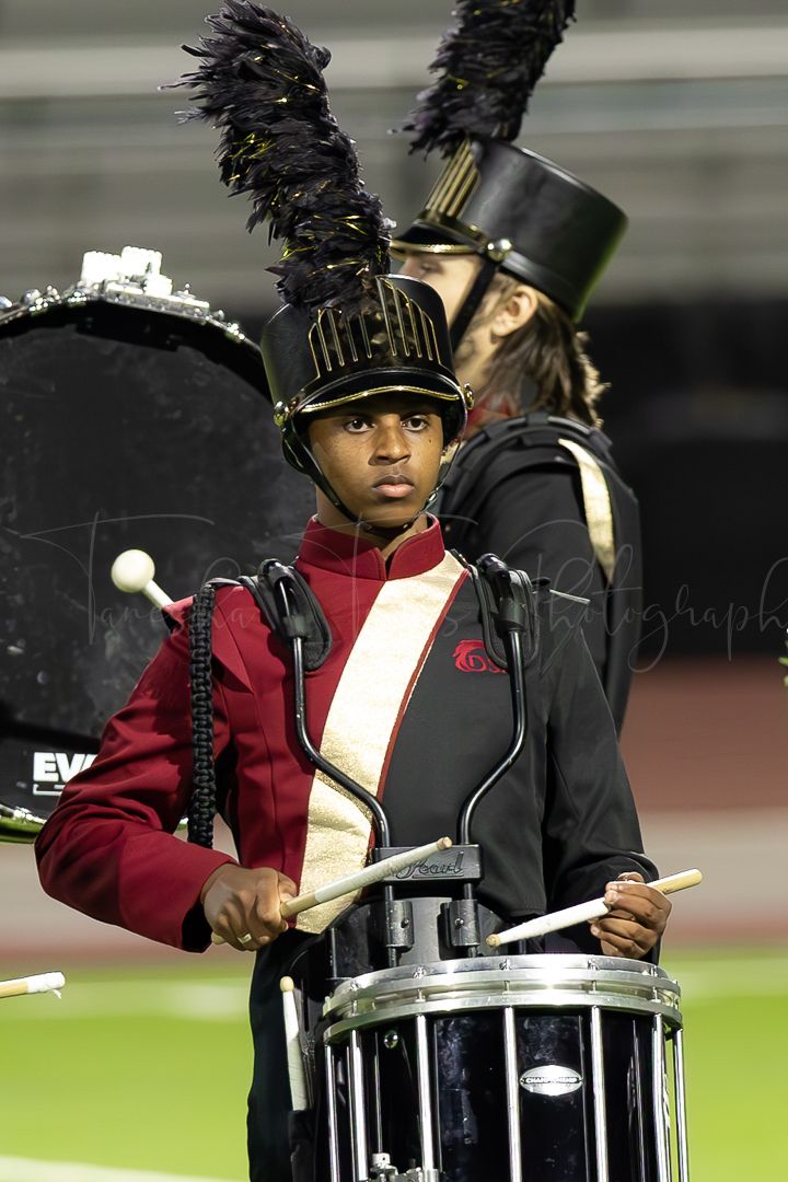 Drummers in marching band uniforms performing on a football field at night.