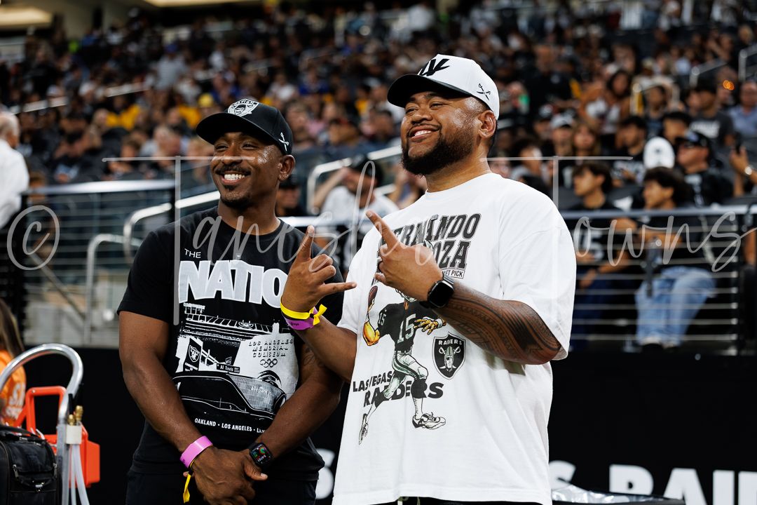 Two Las Vegas Raiders fans smile and pose at Allegiant Stadium during a game.