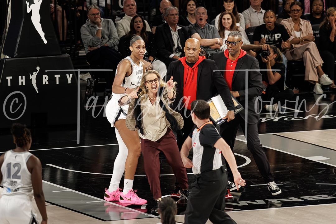 WNBA players and coaches gather on the basketball court during a tense game moment with a referee nearby.