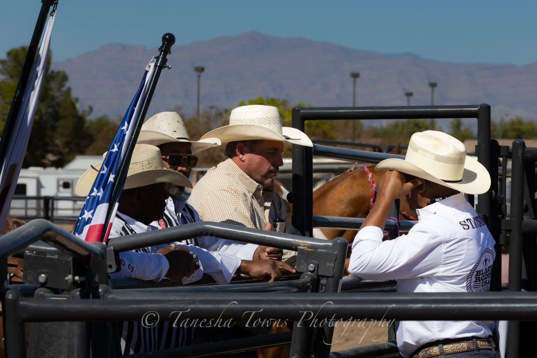 Spectators watch a rodeo event from bleacher seats under a bright blue desert sky.