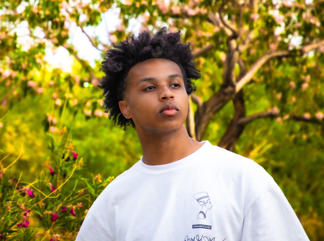 Portrait shot of someone wearing white t-shirt outdoors with natural greenery in background.