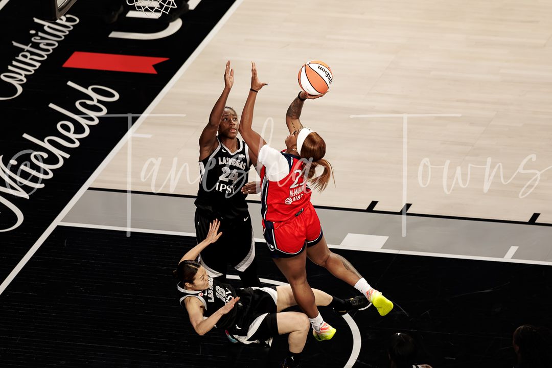 WNBA players compete for the ball during an intense basketball game, with one player shooting over a defender.