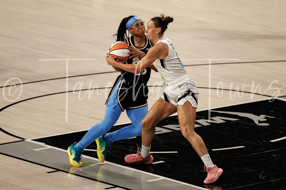 Two WNBA players battle for possession during an intense basketball game, one in blue and one in white uniform.