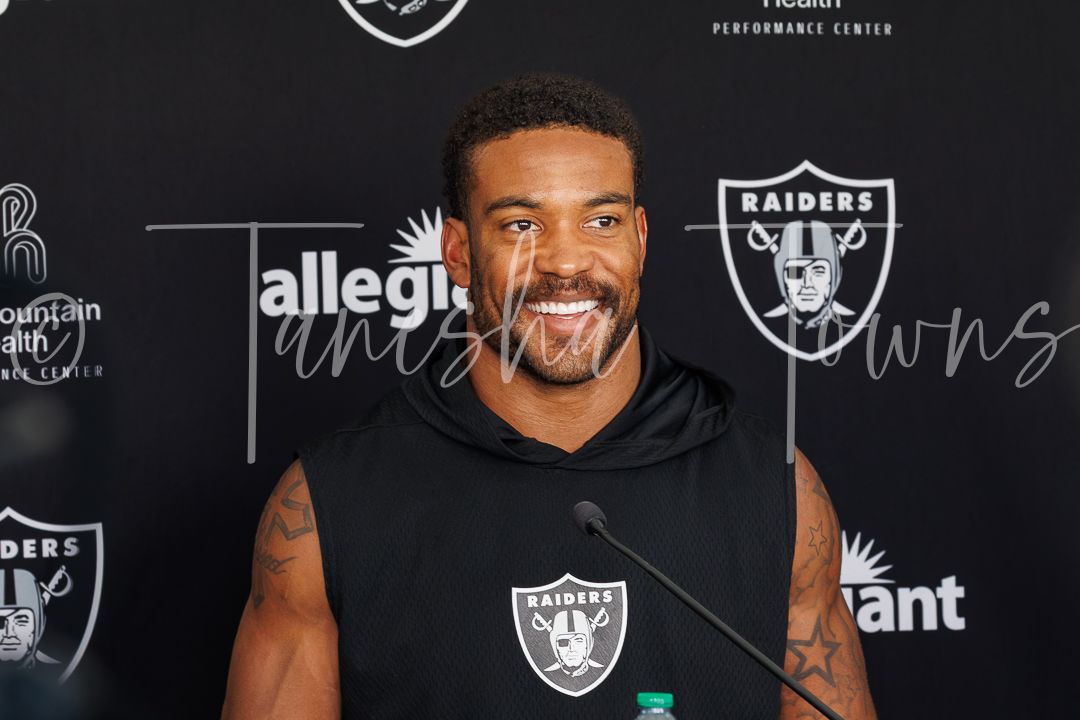 Las Vegas Raiders player smiles at a press conference in front of an Allegiant backdrop.