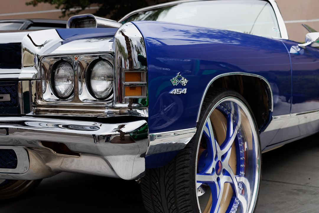 Blue classic Chevrolet 454 muscle car with chrome bumper and custom blue and white rims at a car show.
