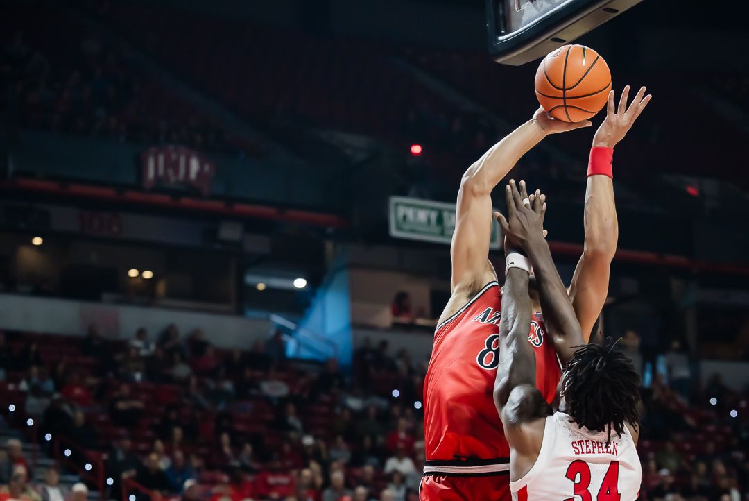 Basketball player rises up for a jump shot during an intense game with defenders nearby.