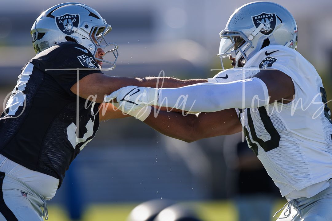 Two Las Vegas Raiders players battle in blocking drill during NFL training camp practice outdoors.