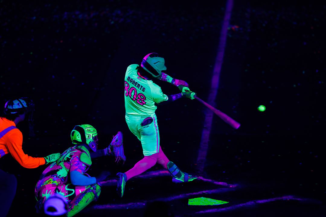Glowing neon baseball player swings bat under black light during a vibrant UV-lit night game event.