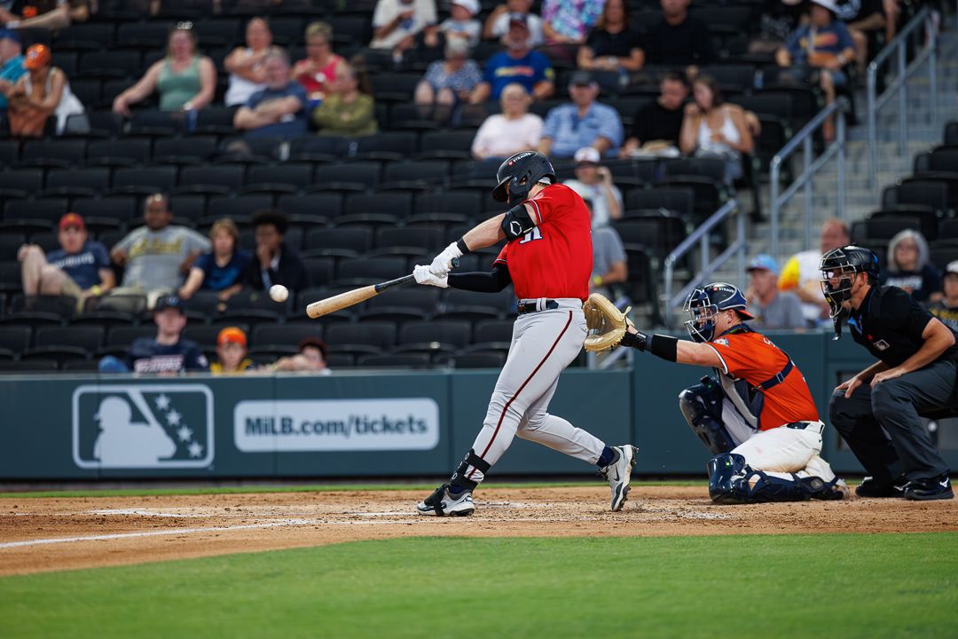 Baseball batter swings at pitch during night game, catcher and umpire behind home plate in MLB stadium.